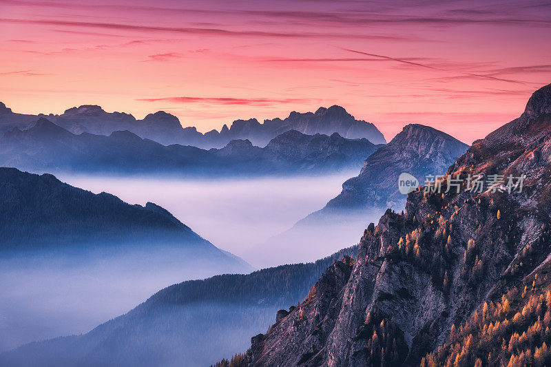 意大利Dolomites的秋天，在美丽的夕阳下，山中的雾。景观有高山山谷，低云，树木在山上，红色的天空与云彩在黄昏。鸟瞰图。航道Giau)。旅行