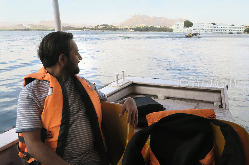 快乐的印度印度男子乘客在旅游游轮上穿着救生衣，橙色救生衣浮在皮霍拉湖，泰姬陵湖宫殿，皮霍拉湖乌代普尔，旅游船夫微笑着，暑假在乌代普尔，游湖的景色