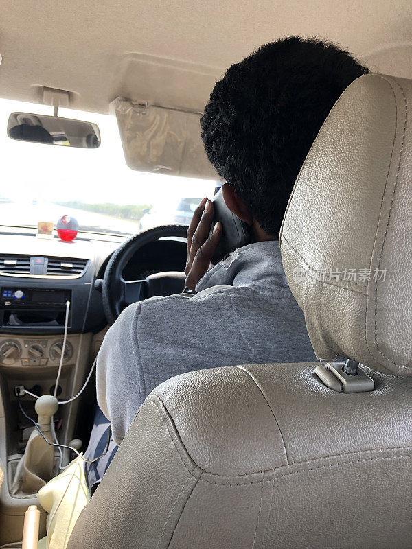 在印度新德里附近，一名印度男子系着安全带在私人出租车上用手机驾驶，这是危险的驾驶照片，司机在使用手机