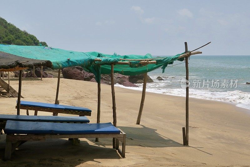 在印度果阿的可乐沙滩上，在水边的空旷的海边日光躺椅上，为保护阳光而建造的简陋遮阳棚