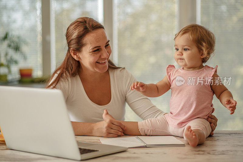 快乐的母亲抱着她的宝贝女儿，她正在电脑上看卡通片