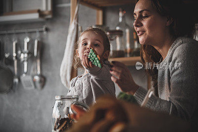 可爱的蹒跚学步的小女孩和她的妈妈在厨房里玩饼干