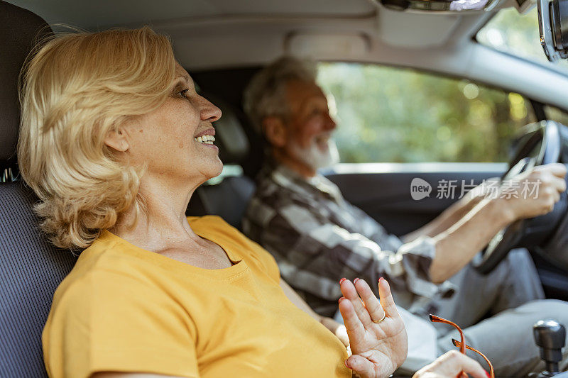 年长的白人驾驶着汽车，他的妻子坐在他的前排座位上，近处，侧视图