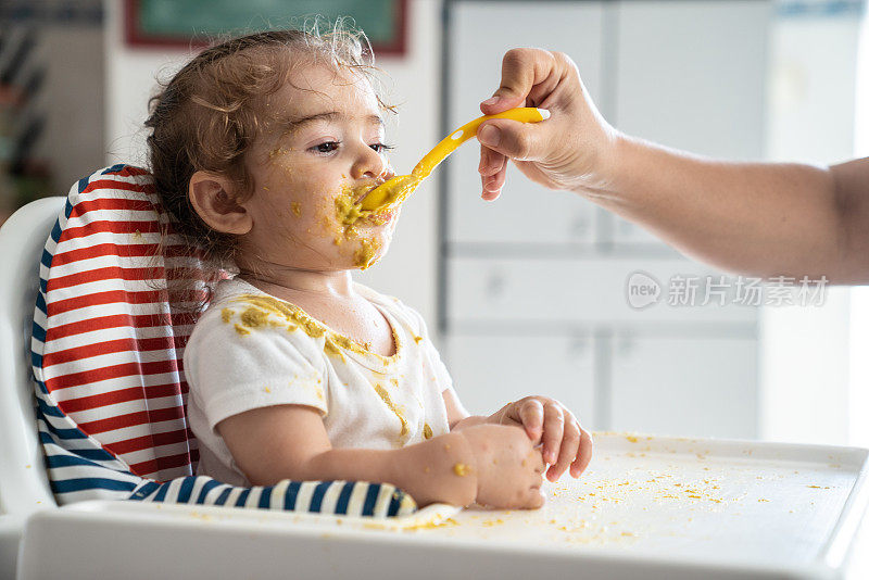 女婴坐在喂食椅上吃婴儿食品