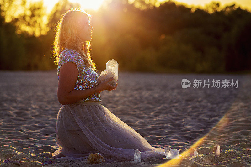 美丽的女人在海滩上拿着治愈水晶