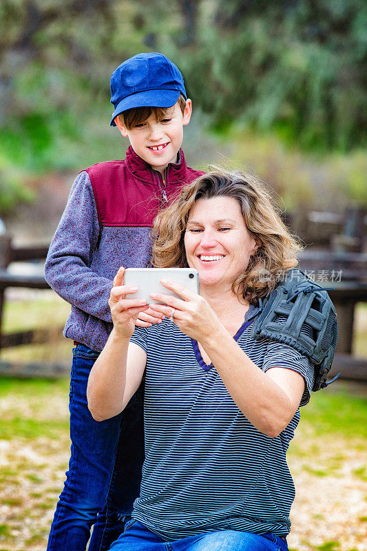 妈妈在户外打棒球时用手机给儿子看了一段视频