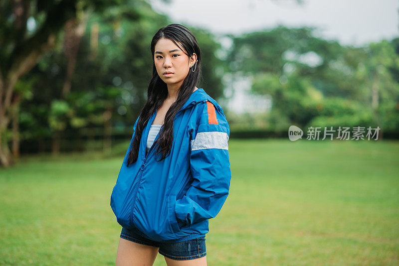 亚洲华裔少女穿着蓝色帽衫站在公园里看着镜头