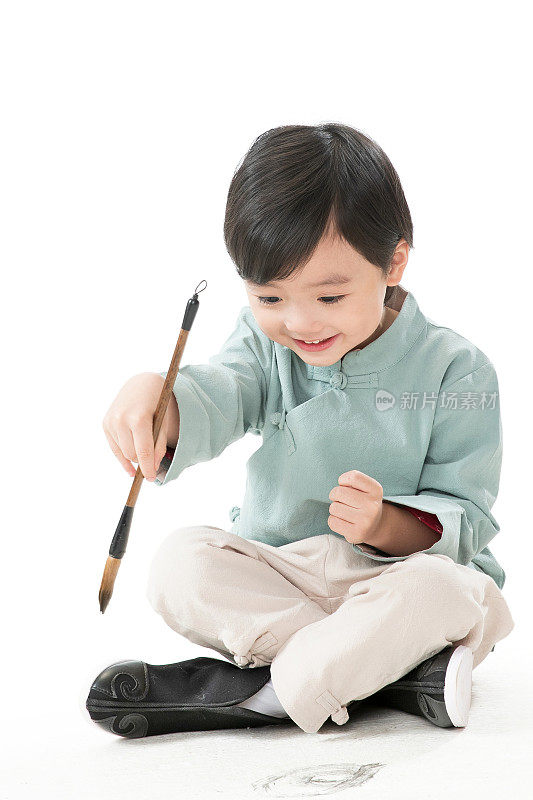 可爱的小男孩坐在地上用毛笔写字