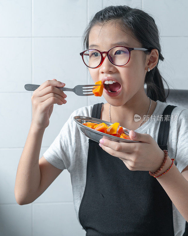 亚洲女孩看着相机吃木瓜的照片