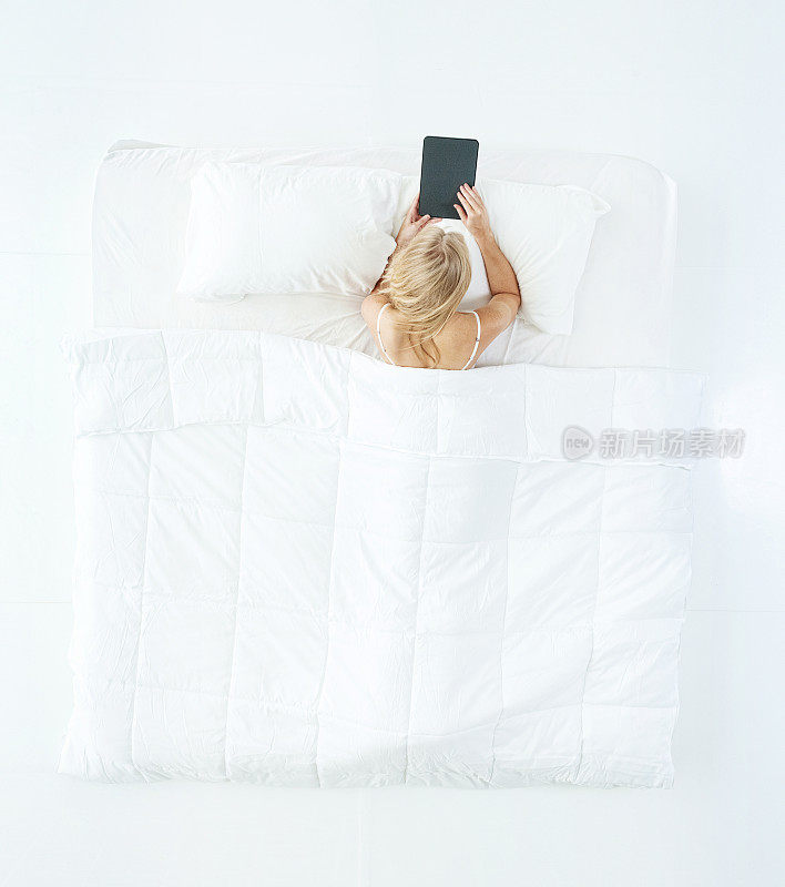白人年轻女性穿着内衣在卧室的白色背景下使用触摸屏睡觉
