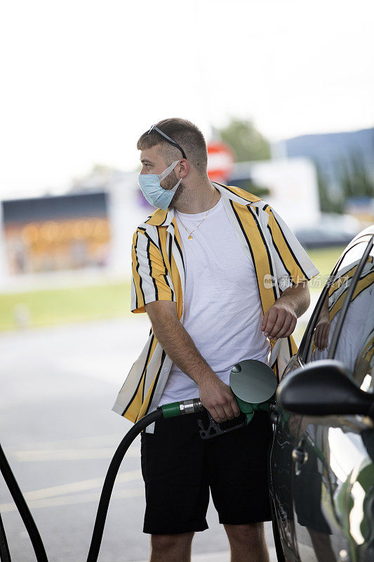 年轻的成年男子戴着防护面具在加油站加油