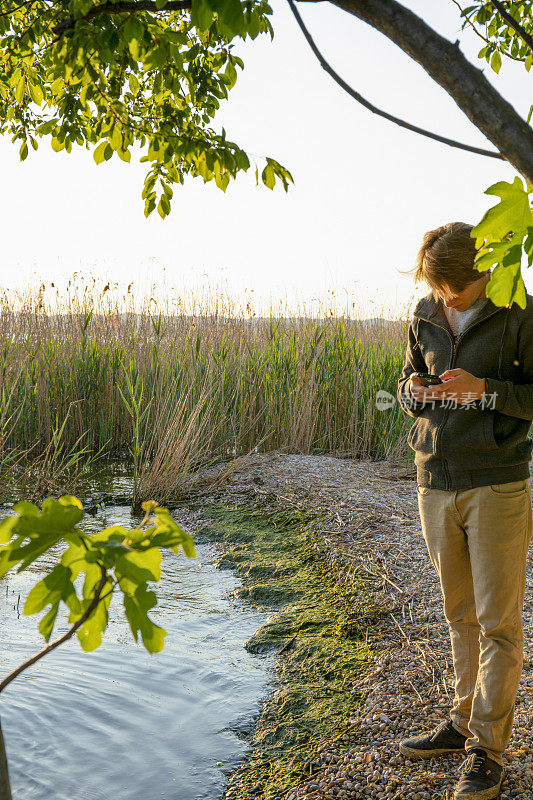 日落时分，一名年轻人在湖边使用手机