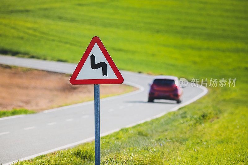 交通标志警告双曲线和红色汽车在路上。