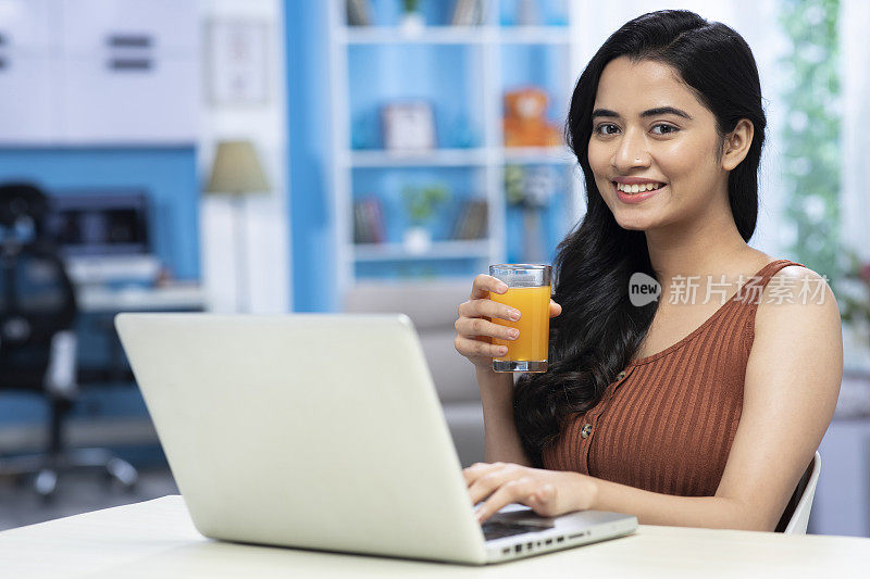 年轻女性使用笔记本电脑和喝橙汁库存照片