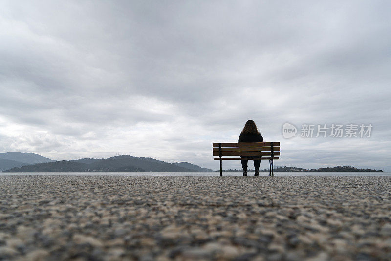 一个超重的年轻女人坐在海边的长椅上看风景