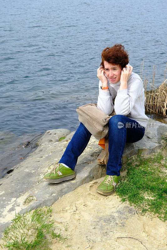 坐在湖边的石头上的女人越来越冷，戴上了她的兜帽