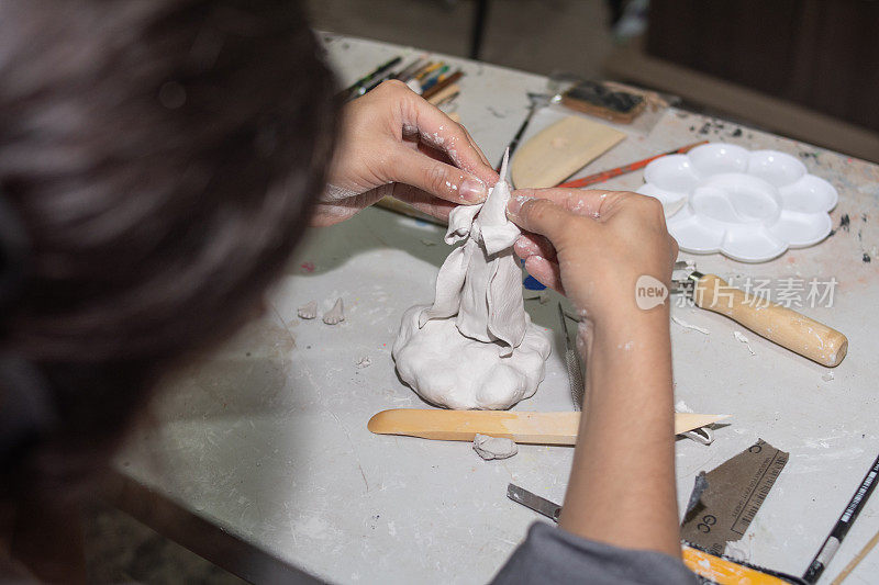工匠的手用粘土和模塑糊在桌子上用几个模塑工具和刷子塑造一个雕塑