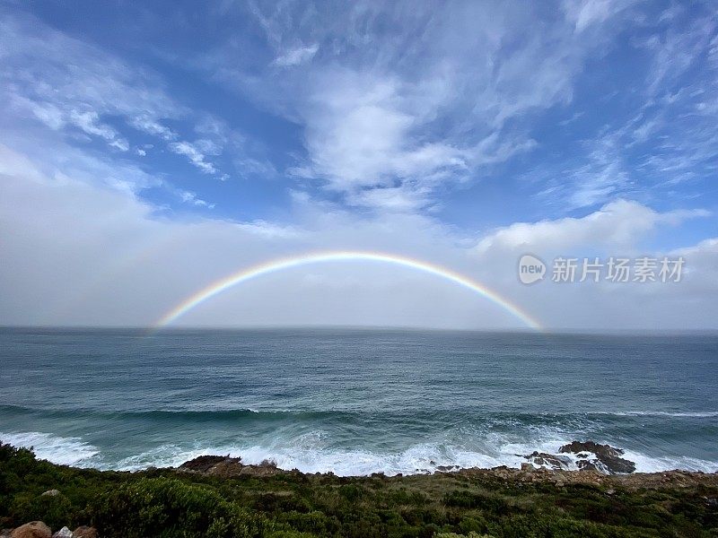 海浪拍打着海岸，背景是彩虹