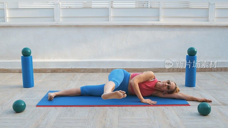 健身妇女侧躺在运动垫上，伸展腿在身体前面
