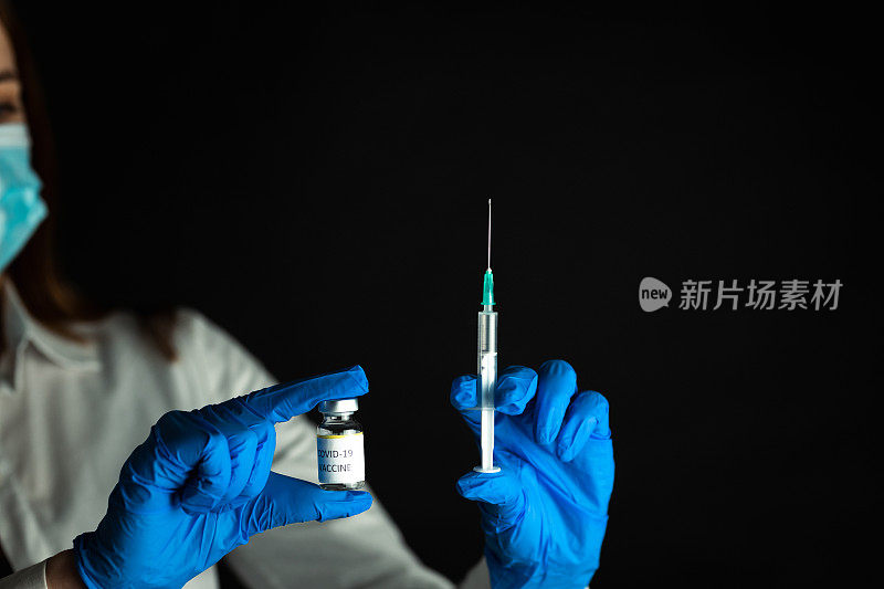 戴着乳胶手套的护士，手里拿着COVID-19疫苗瓶和注射器