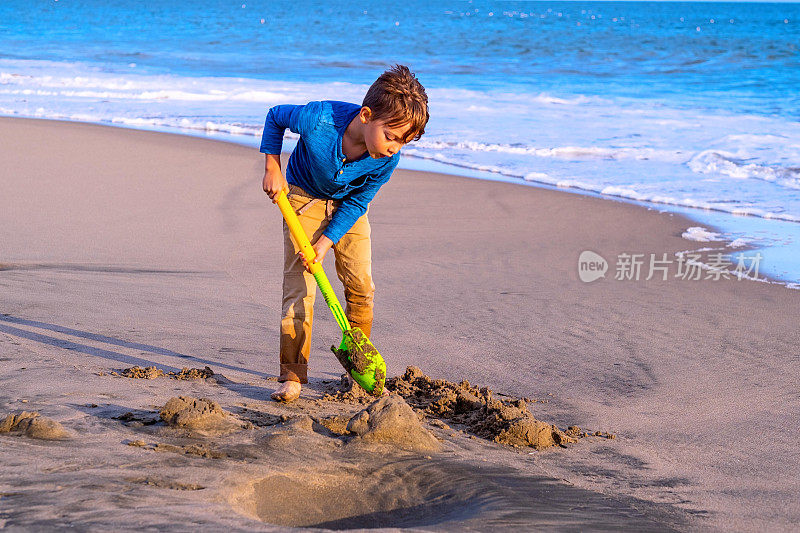 小男孩在沙滩上用铲子在沙地上挖洞