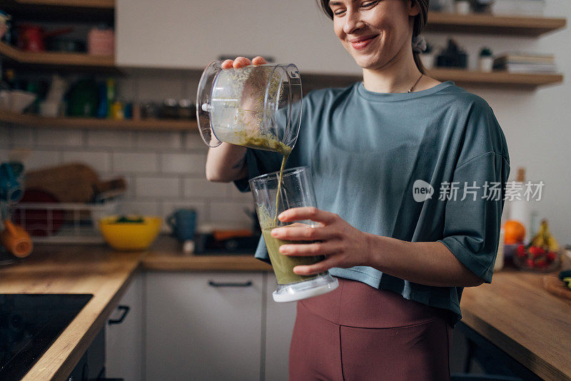 健康的女人把刚做好的奶昔从搅拌机倒进饮水杯