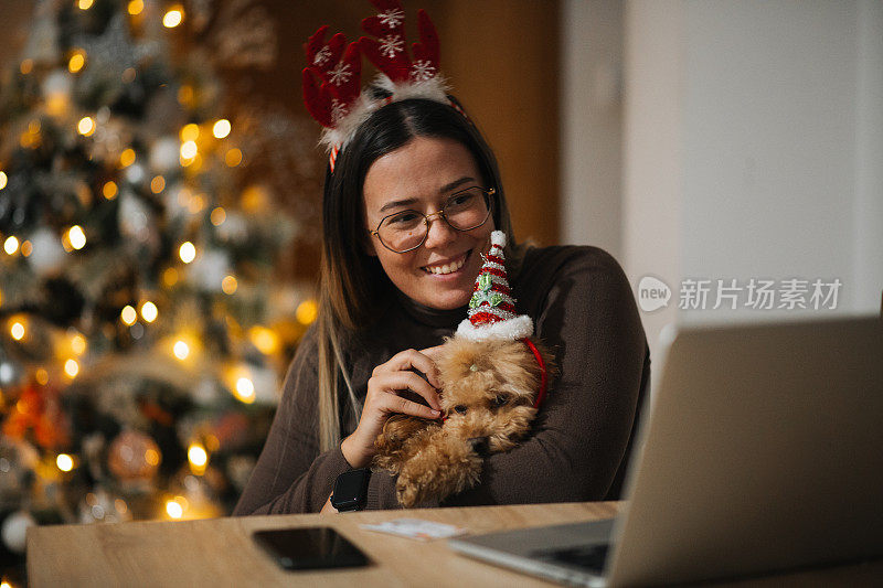 除夕，一名女子和她的宠物狗戴着鹿角发带，在笔记本电脑上看电影