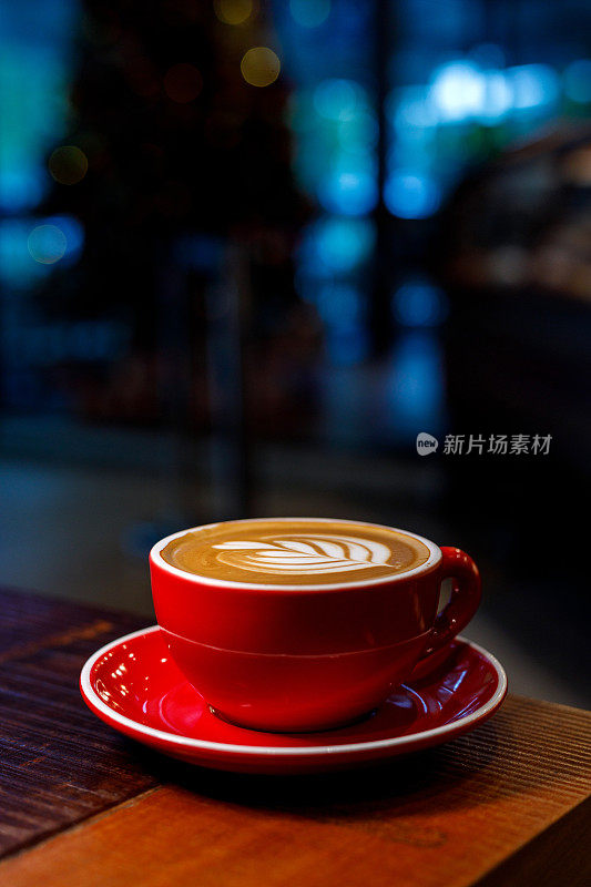 靠近热卡布奇诺红色咖啡杯与心形拉花艺术在咖啡屋深棕色旧木桌，食品和饮料的概念。