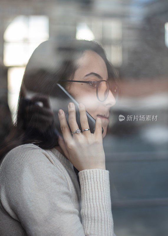 年轻女子在窗户后面讲手机。