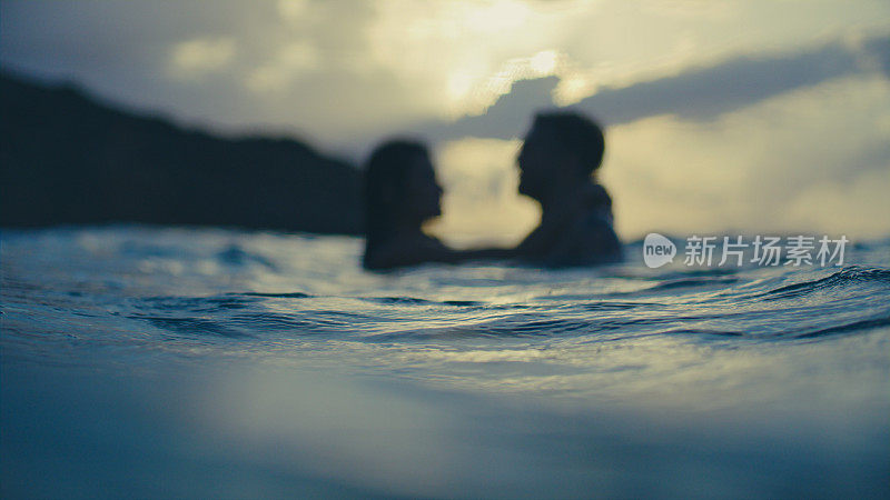 浪漫的异性情侣在金色的夕阳下一起在海里游泳。在水中拥抱