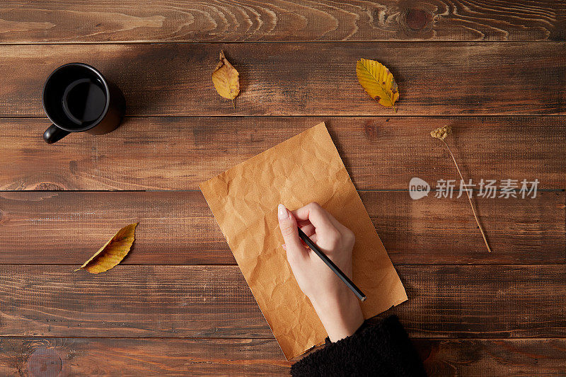 在白纸上写字。木制背景与一杯咖啡和秋叶。