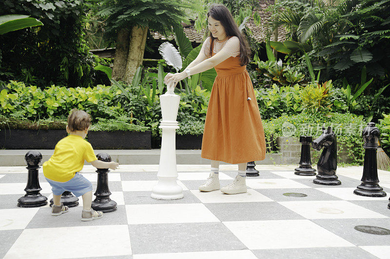 一名亚洲妇女和她的孩子在公园里下巨型国际象棋