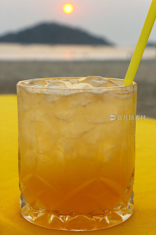 特写图像的海滩餐厅酒吧场景，喝一杯龙舌兰日出鸡尾酒饮料与冰和柠檬片布覆盖的桌子，重点在前景