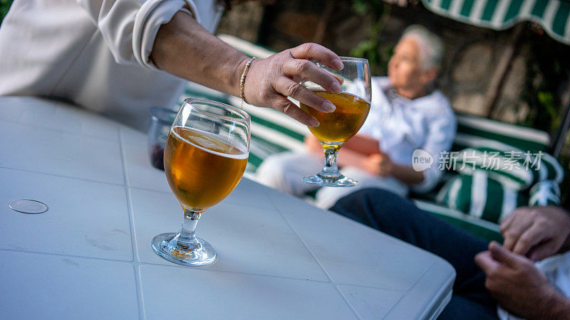 女人手里拿着啤酒杯放在桌子上聚焦前景，成熟的女人则是背景在花园横向的家庭活动