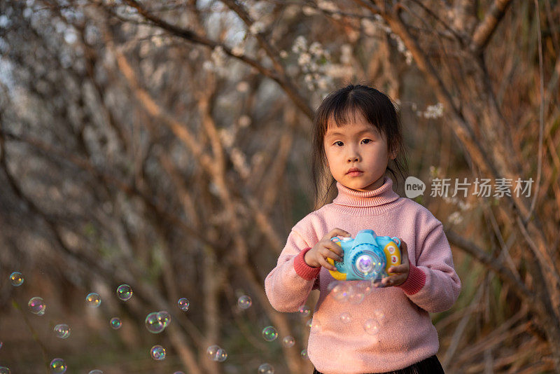 一个小女孩在梅园里用玩具吹泡泡