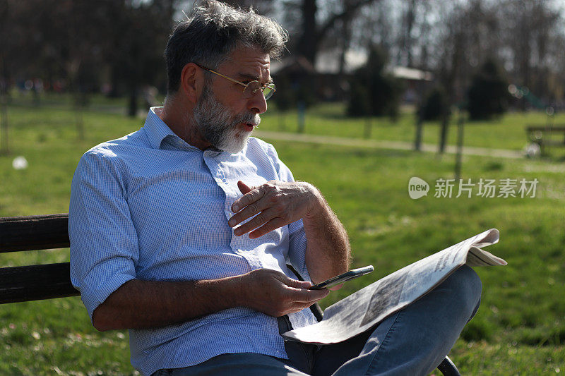 一个成熟的男人坐在长凳上看报纸