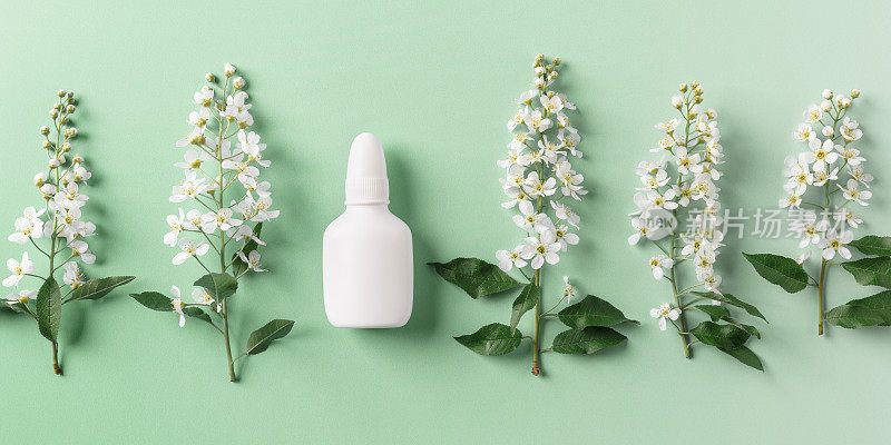 季节性的春季过敏，春天的树枝树上有白色的花朵和绿色背景上的模拟鼻喷雾剂瓶，过敏的概念开花。抗组胺喷雾剂用于鼻塞