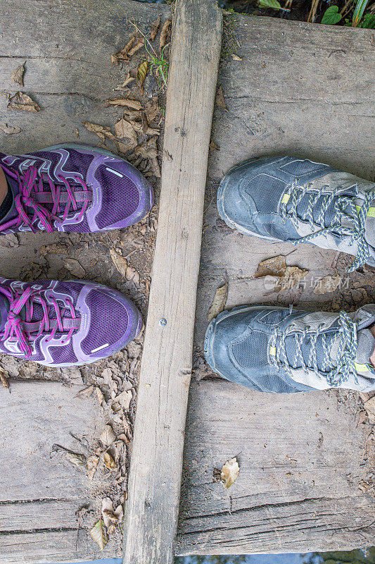 女士的登山鞋在男士的登山鞋前面，在一座自然的木桥上