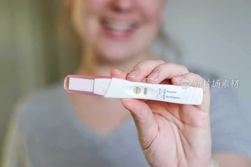 一个快乐的女人拿着怀孕测试呈阳性的特写