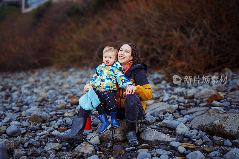 母亲和蹒跚学步的儿子坐在岩石海岸线上