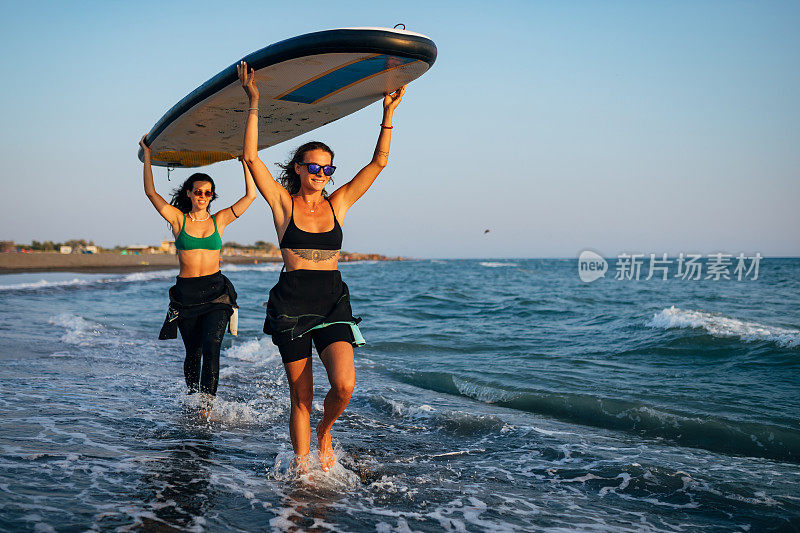 两个女冲浪者准备冲浪。他们进入海水时，脸上的表情都很满意。