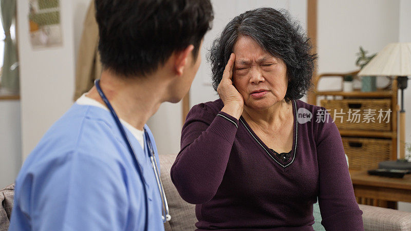 在家访期间，一名沮丧的亚洲老年女性正与心理治疗师交谈。她头痛得厉害，会诊时捂着脸