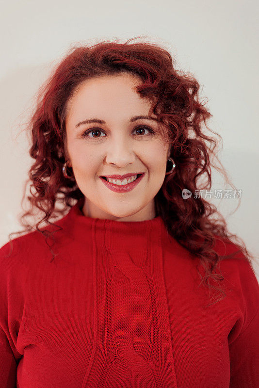 年轻美丽的红发女子肖像，穿着红色套头衫，在镜头前广泛微笑