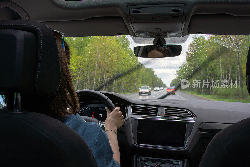 一名女子在雨中驾驶一辆汽车在穿越森林的多车道高速公路上行驶