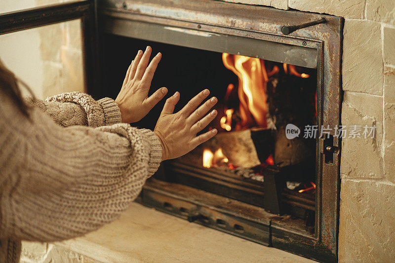 冬天用烧木头的炉子给房子供暖。在农舍的乡村房间里，妇女在燃烧的壁炉前暖手。壁炉取暖，可替代煤气和电