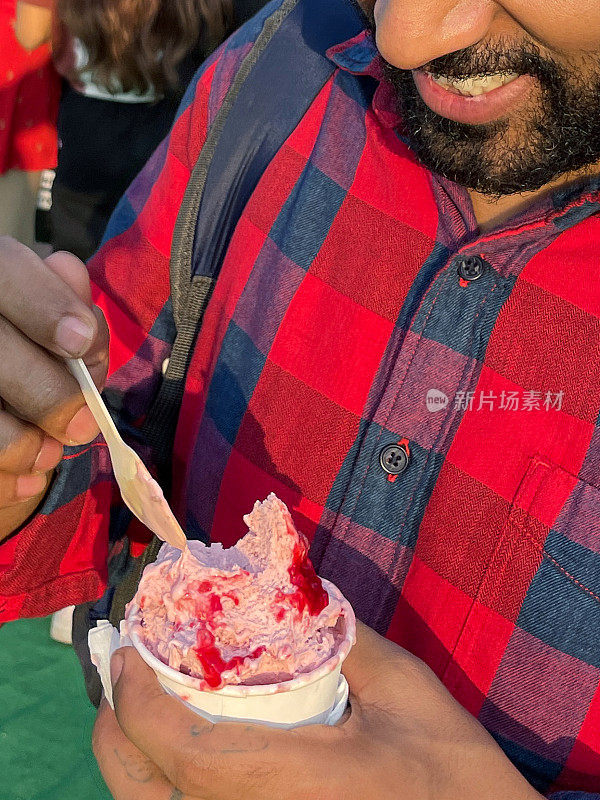 全画幅照片，一个认不出来的人拿着一次性的草莓和覆盆子冰淇淋和浆果水果糖浆，用木勺吃，餐巾纸，专注于前景
