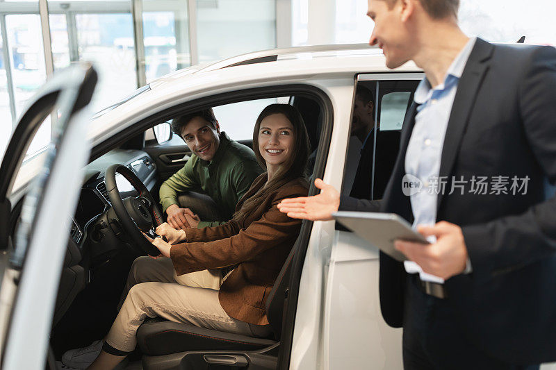 在经销商中心试驾后，千禧一代汽车销售员与快乐的年轻夫妇讨论购买新车