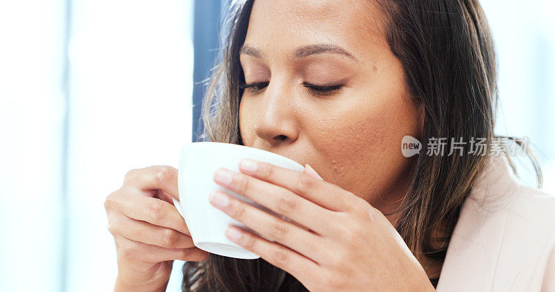 女人在家里喝一杯热茶或咖啡。一个无忧无虑的年轻女性的脸，闻着新鲜的热饮的香气，在家里喝一口，放松一下。享受舒适的休息