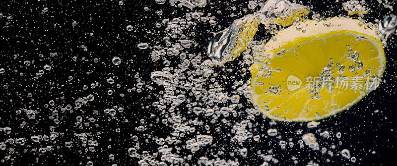 水下鲜榨的甜柠檬水，生柠檬片落在苏打水中，深蓝色或黑色的背景。近景柠檬水或高球柠檬鸡尾酒清凉饮料