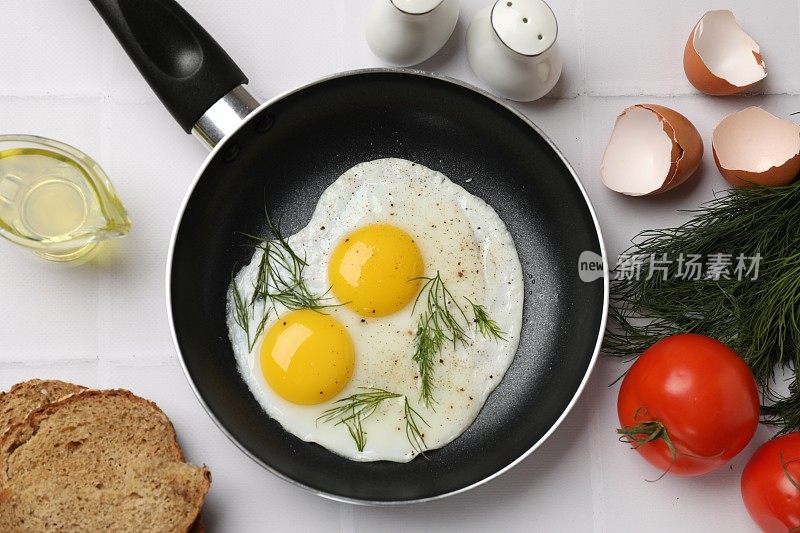 用煎锅将美味的煮熟的鸡蛋、莳萝等产品放在白色的瓷砖桌上，平铺